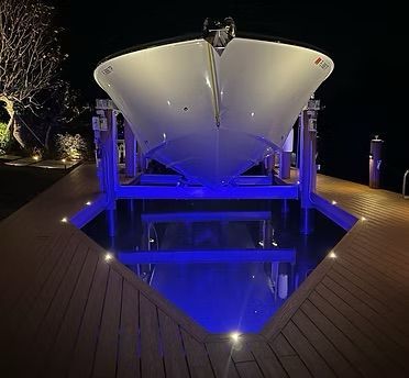 Boat on a lift over water at night; blue lights illuminate the water and underside of the boat.