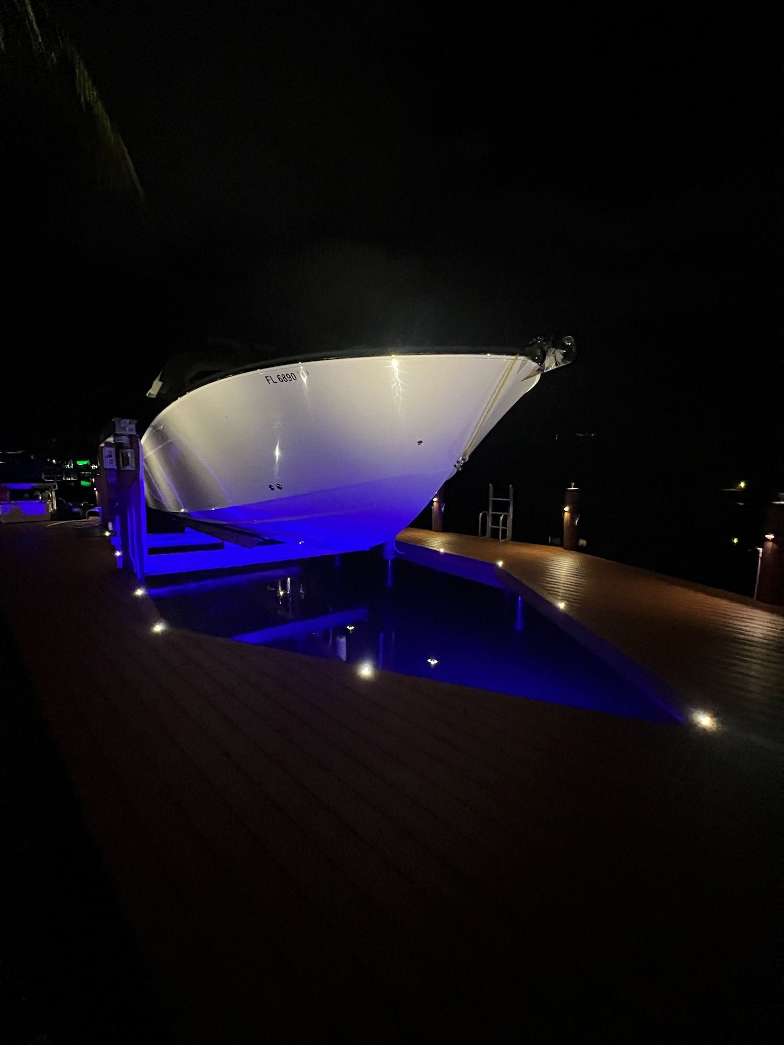 A large yacht at night, lit with blue and white lights, docked at a wooden pier.