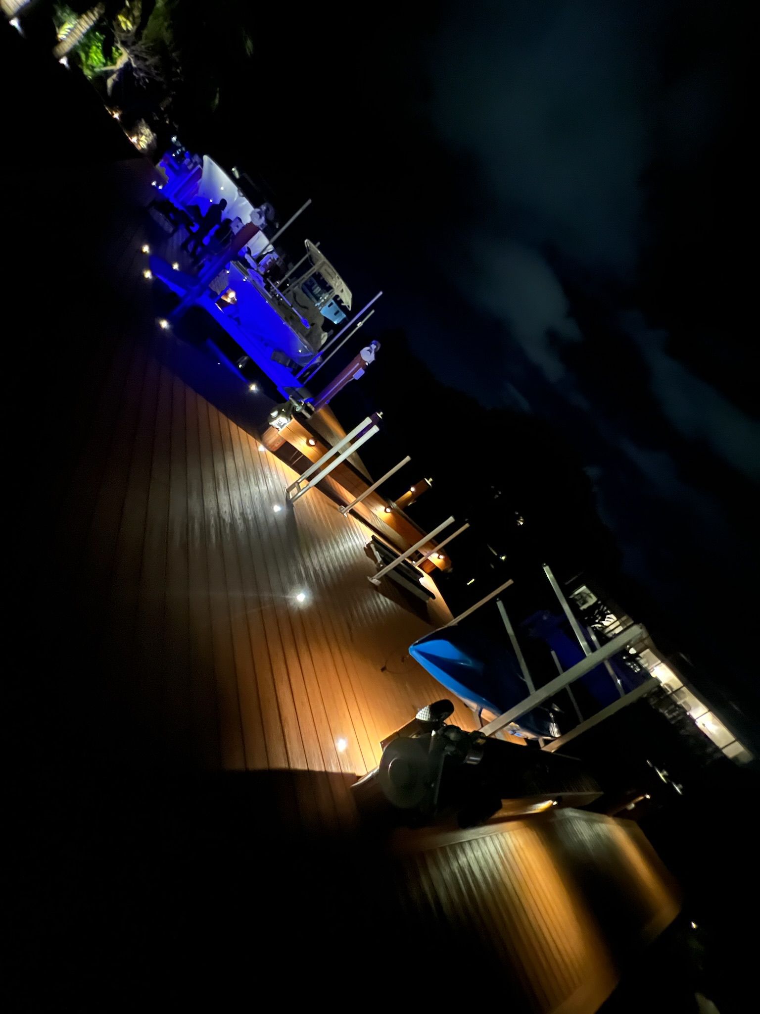 Night view of a marina with illuminated boats and docks; blue and orange lights reflect on the water.
