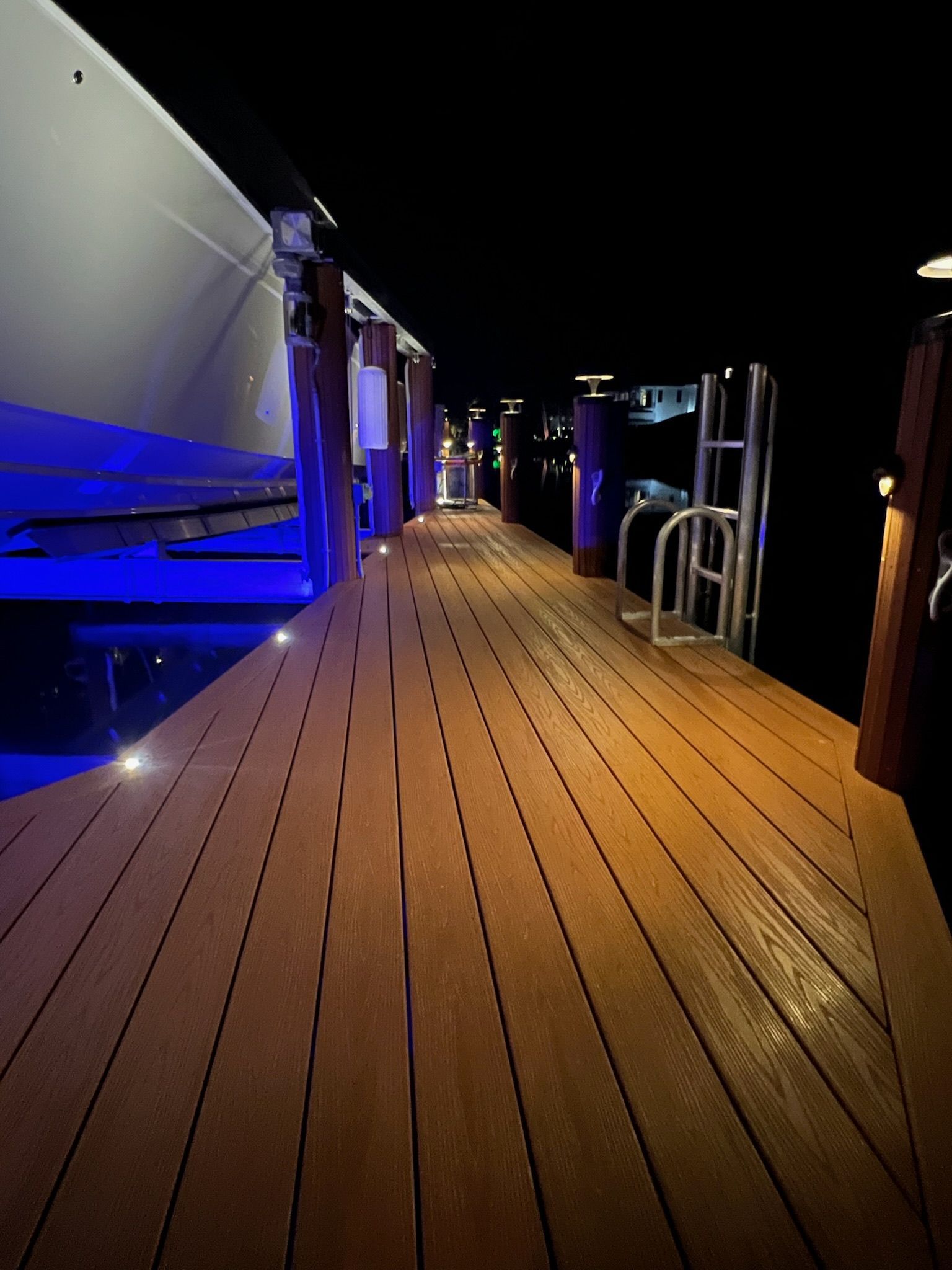 Wooden dock illuminated at night, next to a yacht.