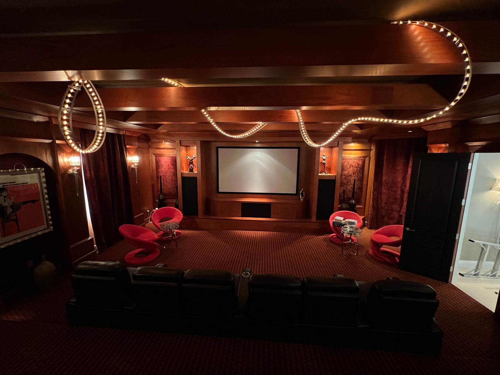 Home theater with a screen, seating, and decorative lights. Red and wood tones dominate the space.