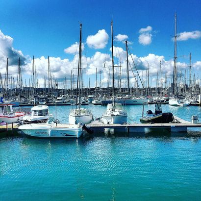 Aerial view of boats docked in marina with one boat moving on teal water.