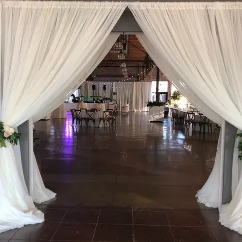 A hallway with white curtains leading to a room with tables and chairs