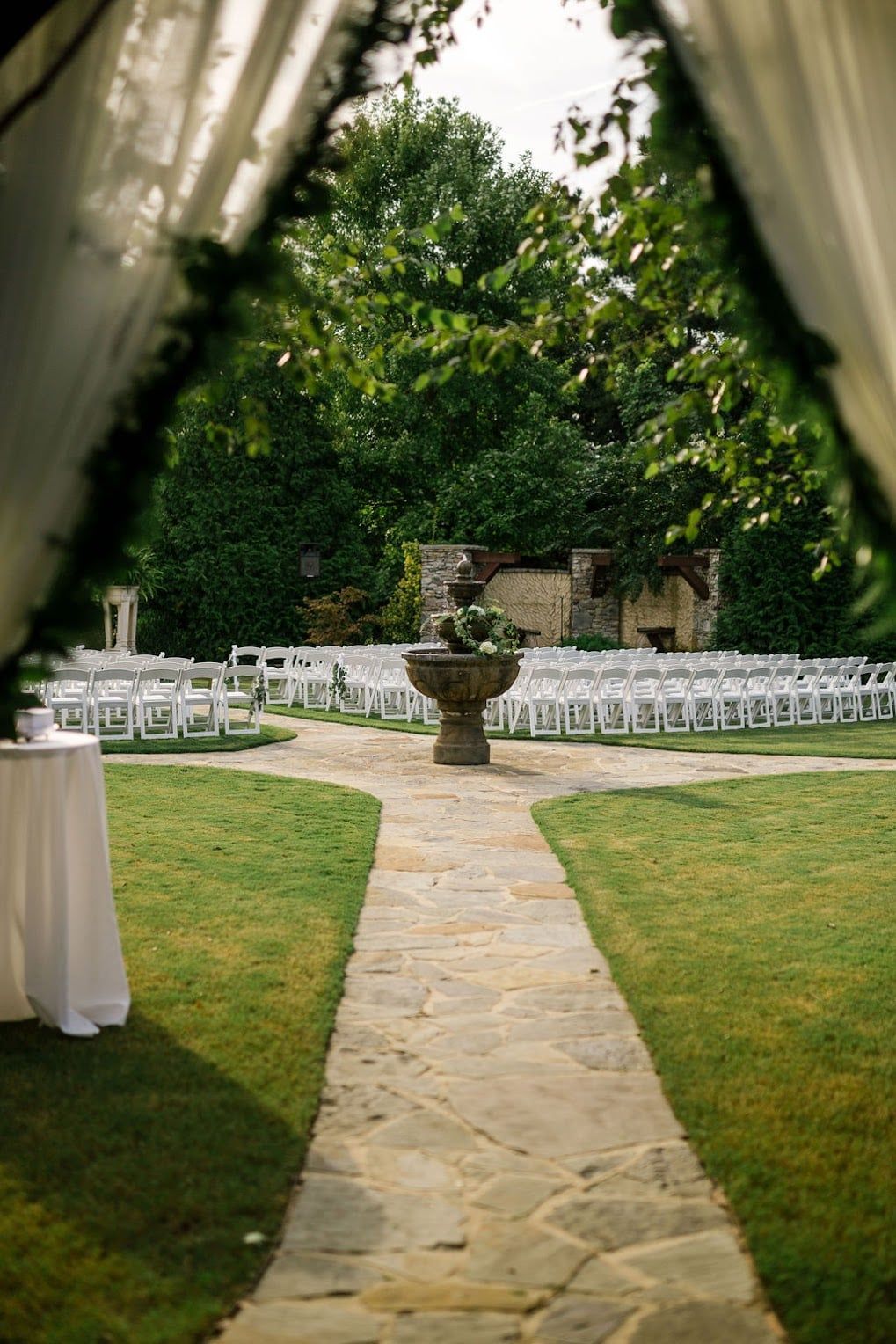 A stone walkway leading to a fountain in the middle of a lush green field.