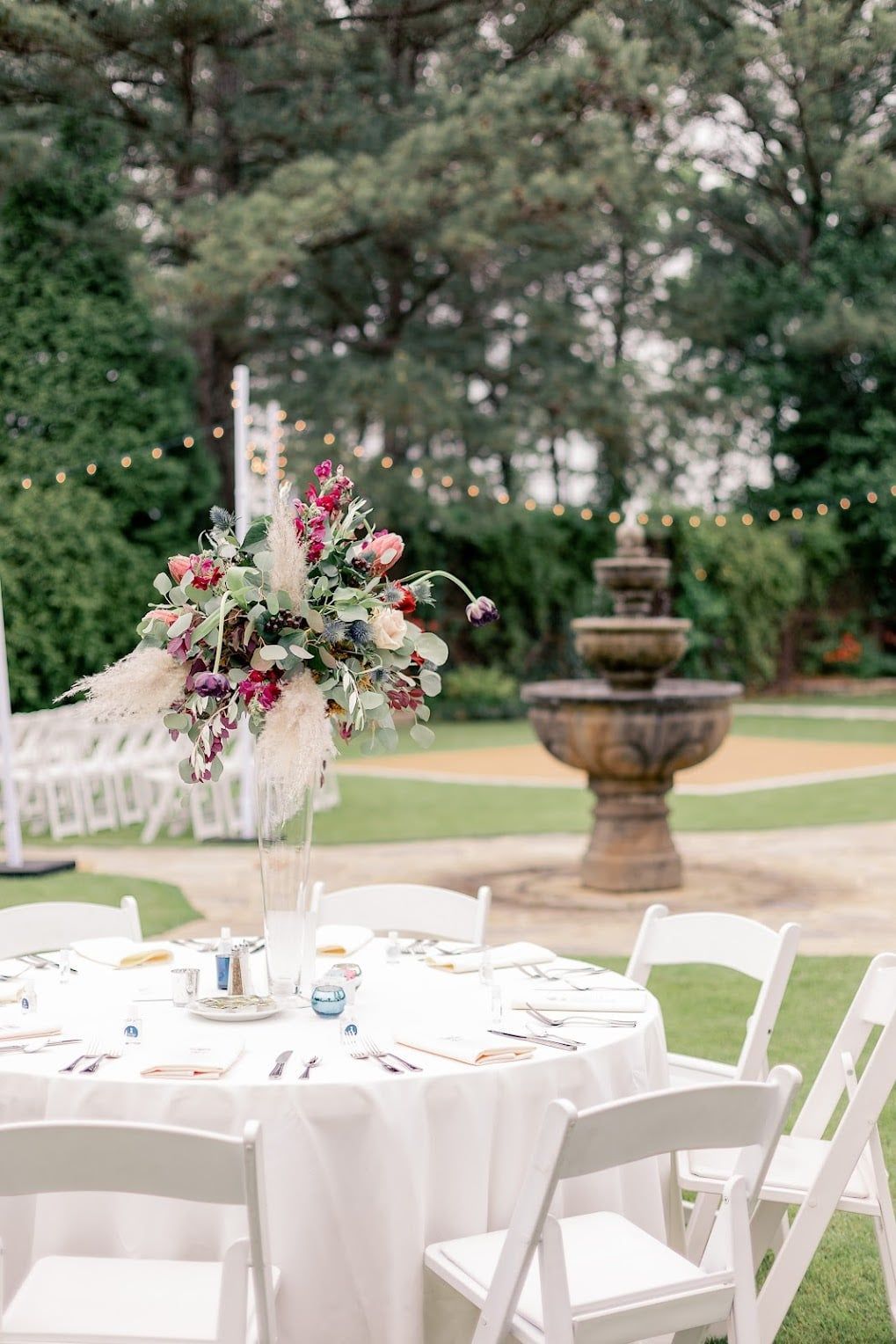 A table and chairs set up for a wedding reception in front of a fountain.
