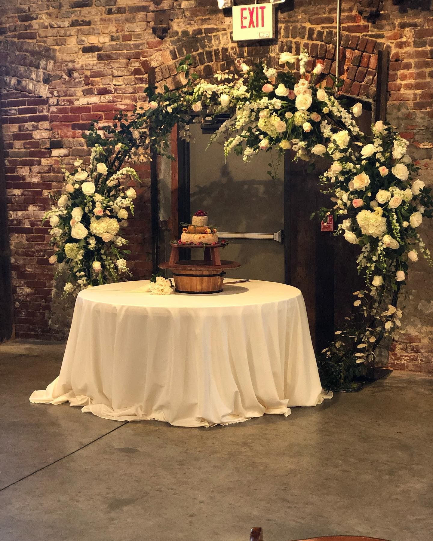 A table with a white tablecloth and a cake on it in front of a brick wall.