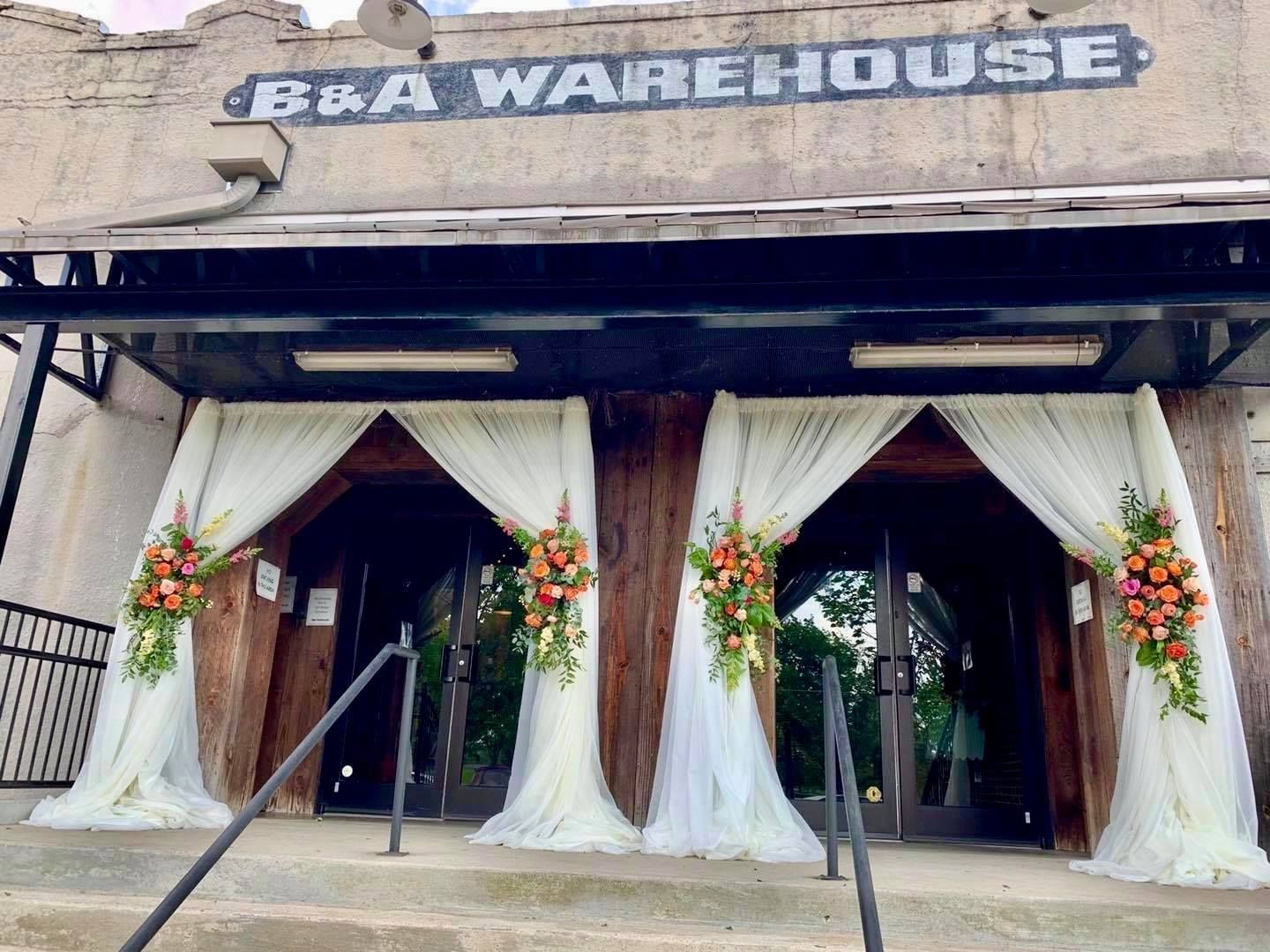 The entrance to the b & a warehouse is decorated with white curtains and flowers.
