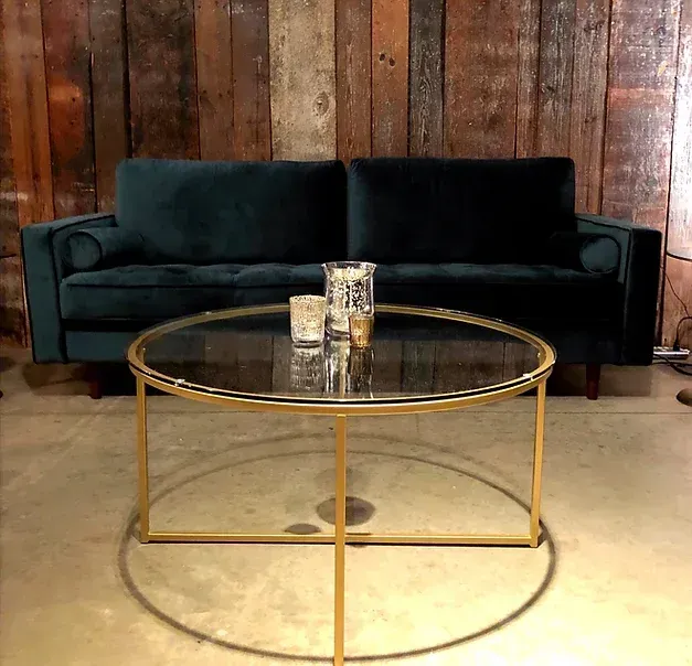 A green couch is sitting next to a round glass coffee table.