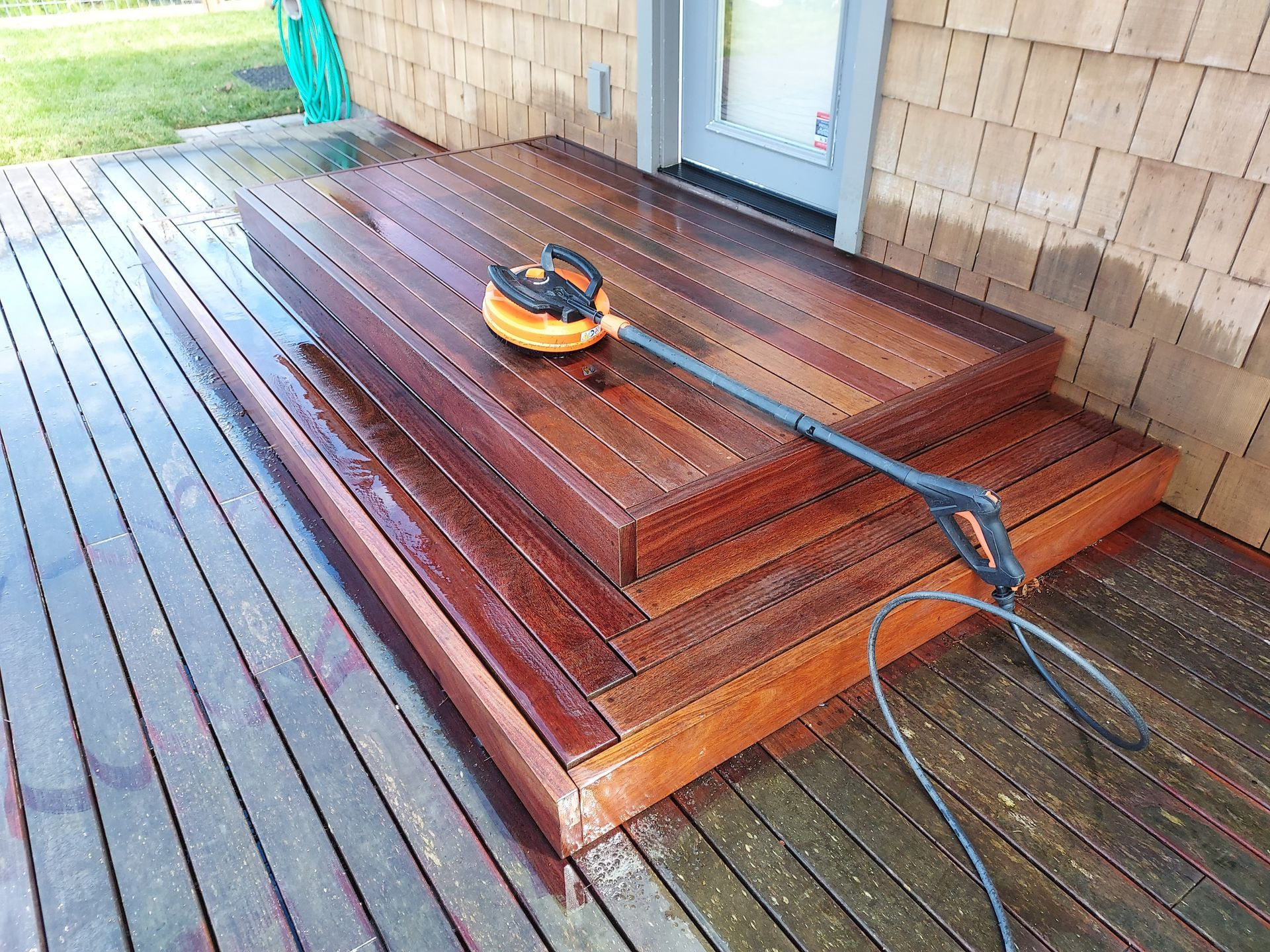 A person power washing a wooden deck and steps; wet wood is dark brown.