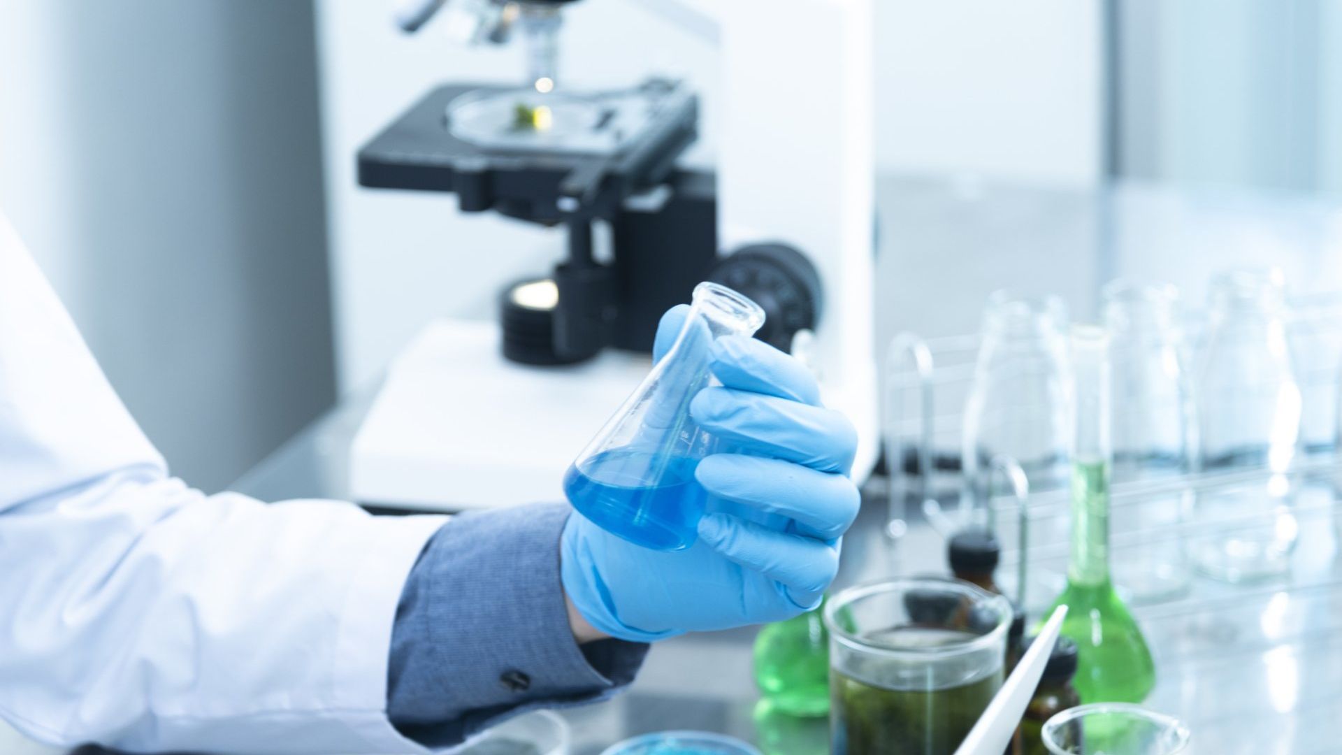 Gloved hand holding a flask of blue liquid in a science laboratory