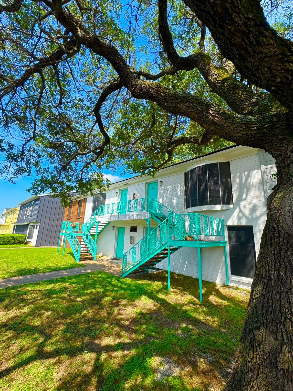 A white house with blue stairs and a tree in front of it.