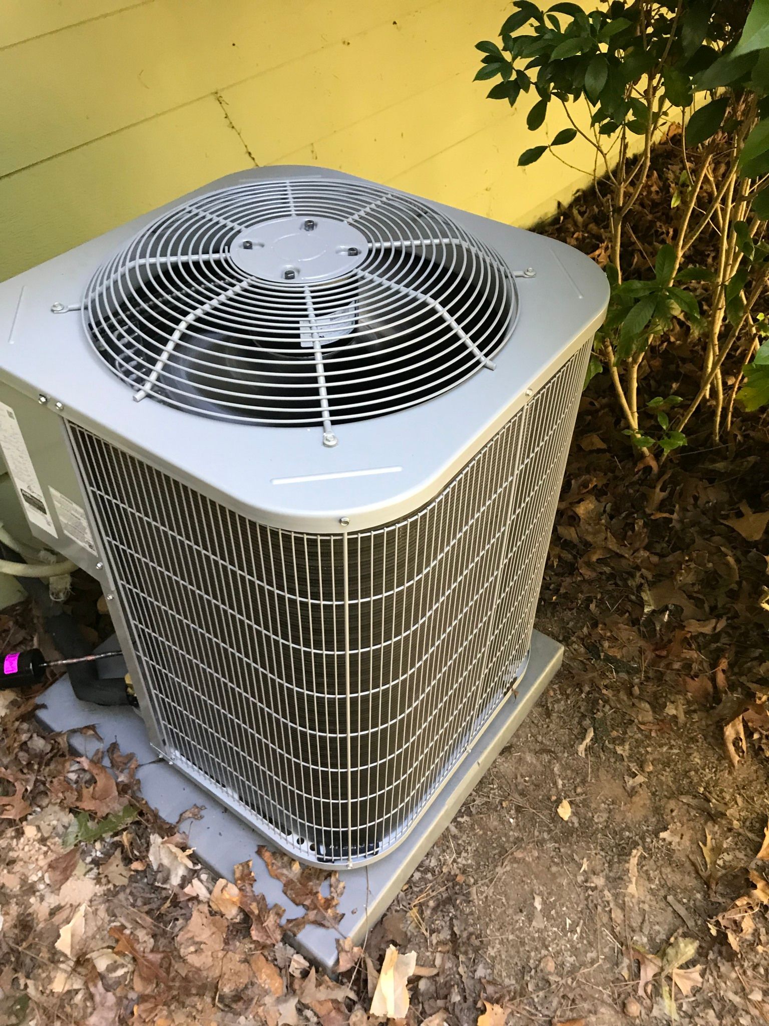 A large air conditioner is sitting on the ground next to a tree.