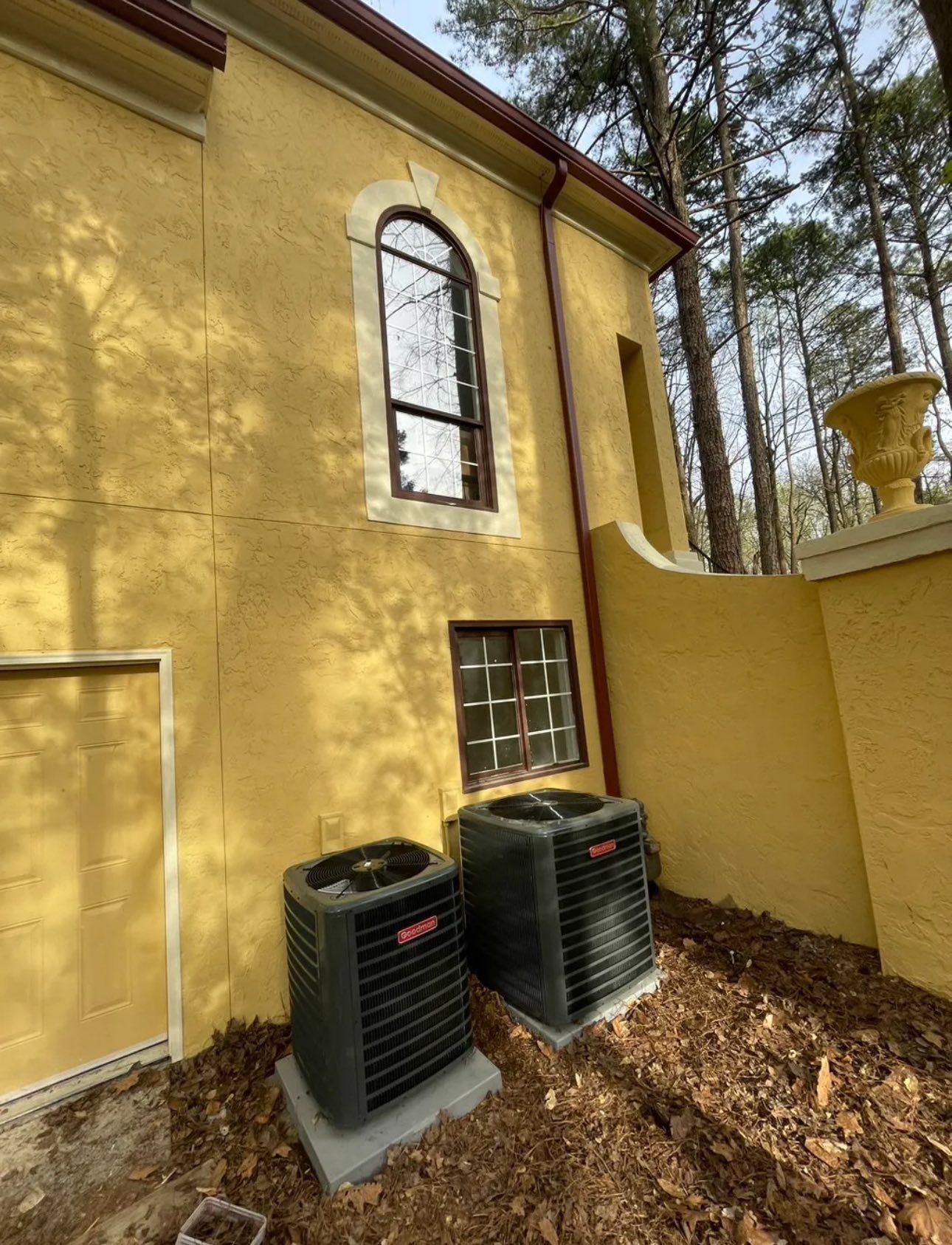 Two air conditioners are sitting in front of a yellow building.