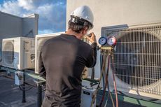 A man is working on an air conditioner on the roof of a building.