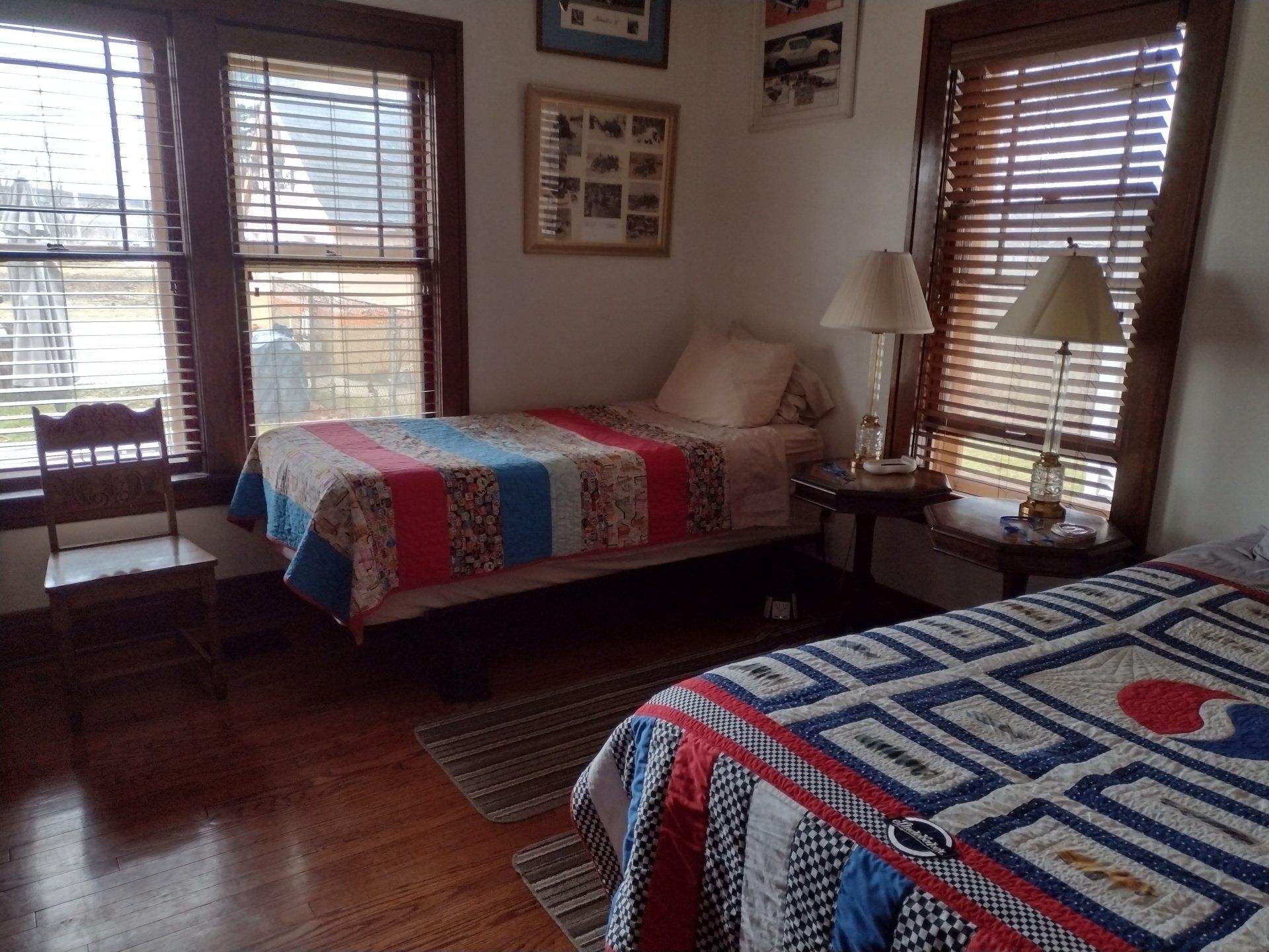 Bedroom with two beds, wood floors, quilts, and window blinds.