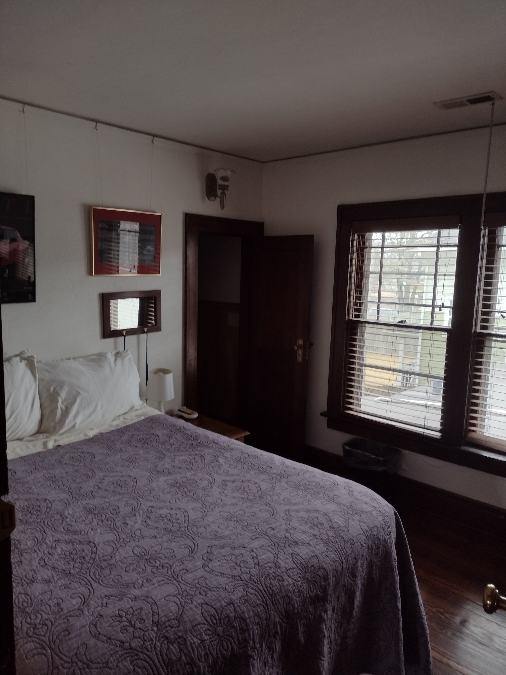 Bedroom with bed covered in a purple floral quilt, a window with blinds, and a dark wood door.