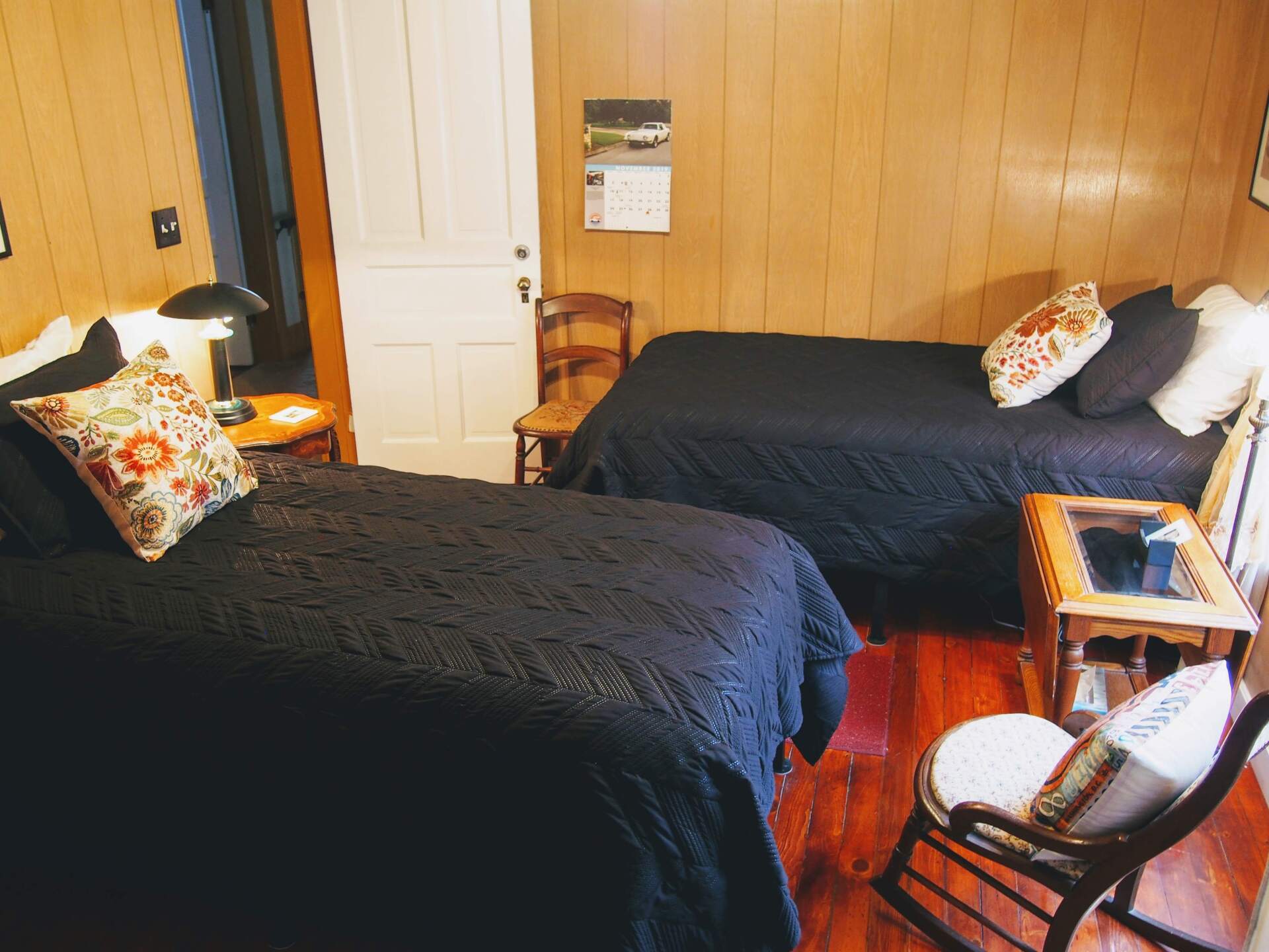 Two beds in a room with wood-paneled walls. Black bedspreads, patterned pillows, and small tables.