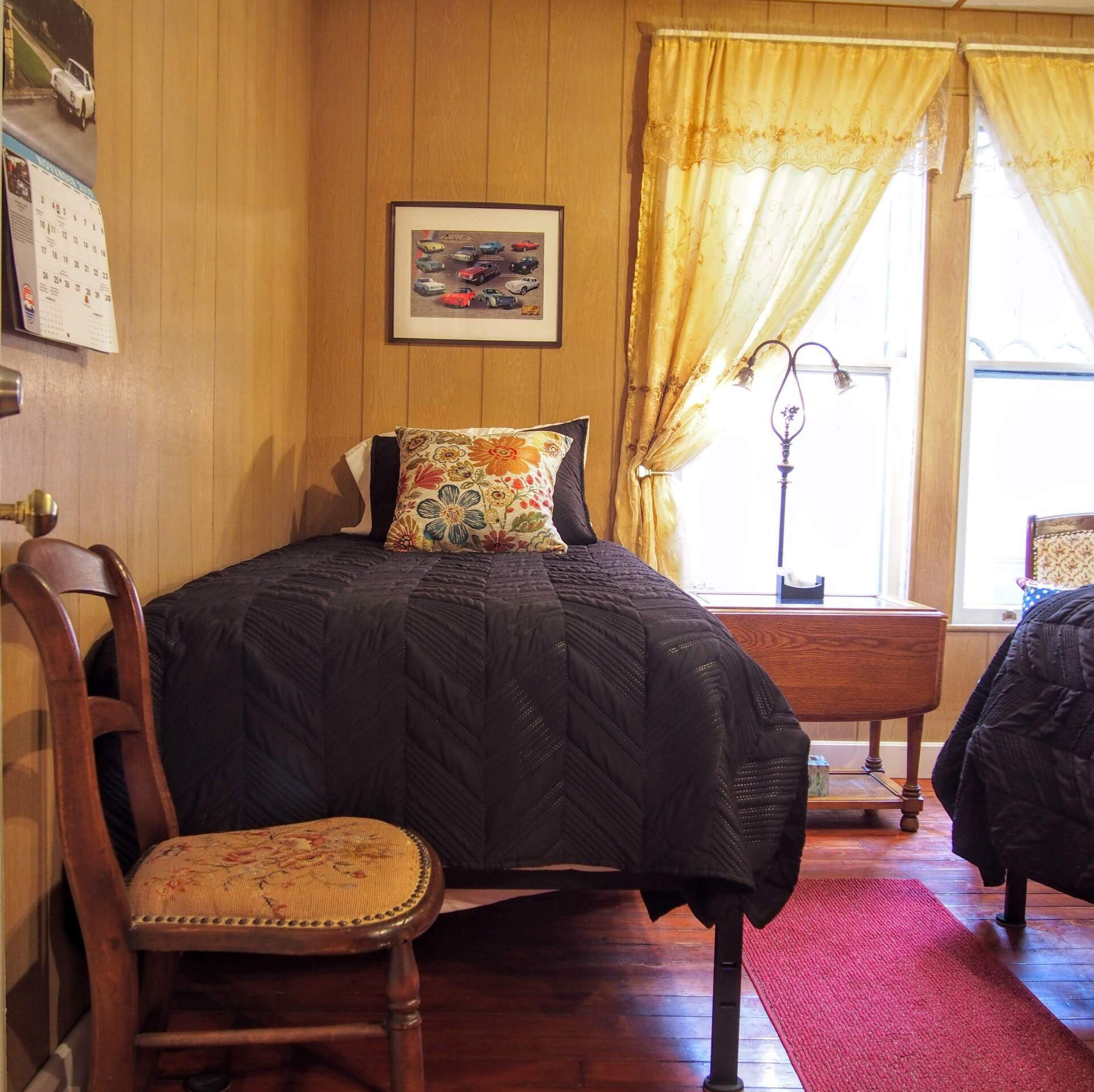A cozy bedroom with two beds, warm-toned wood paneling, and a window with gold curtains.
