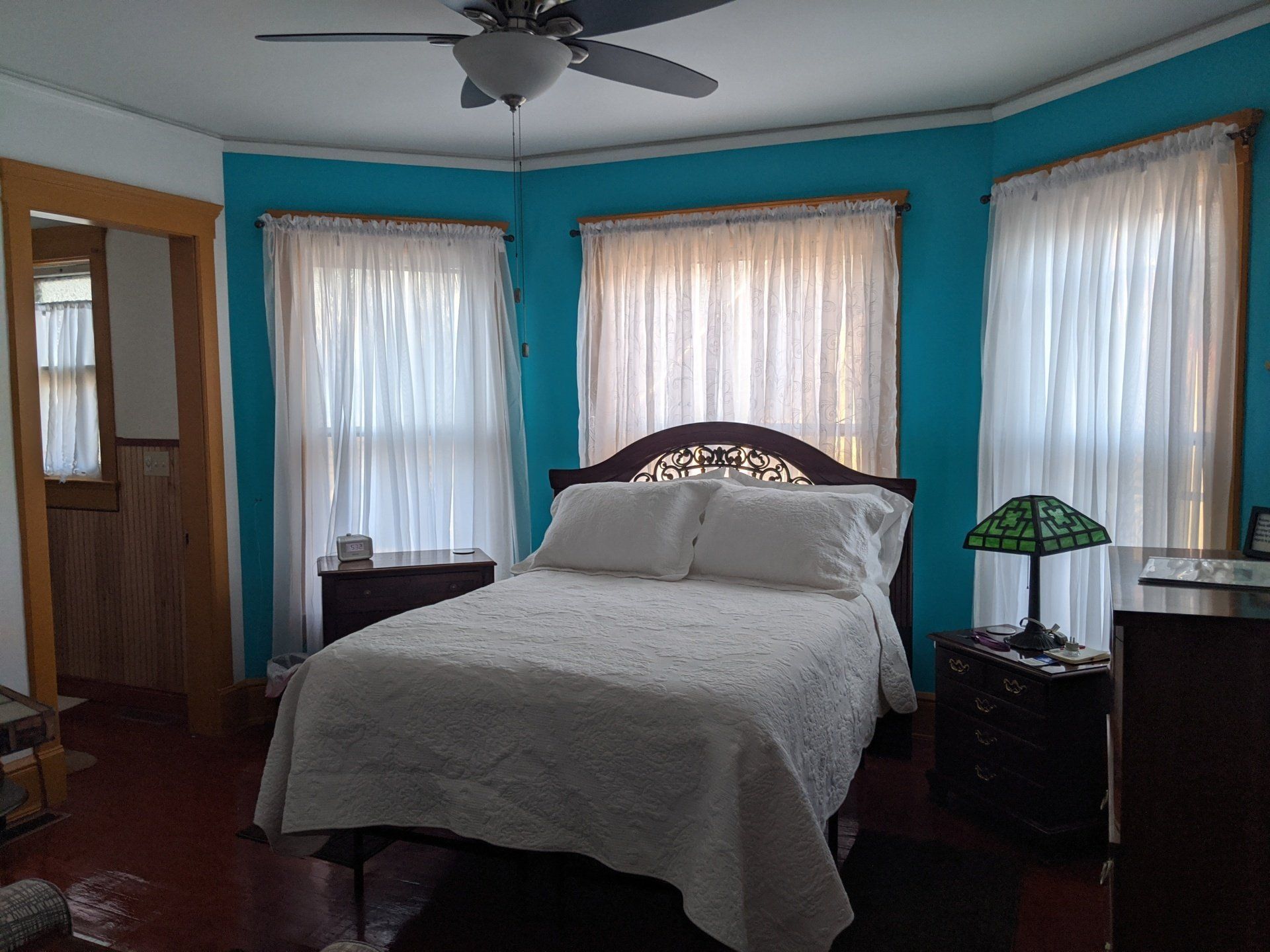 Bedroom with turquoise walls, white bedding, and sheer curtains. A bed is centered.