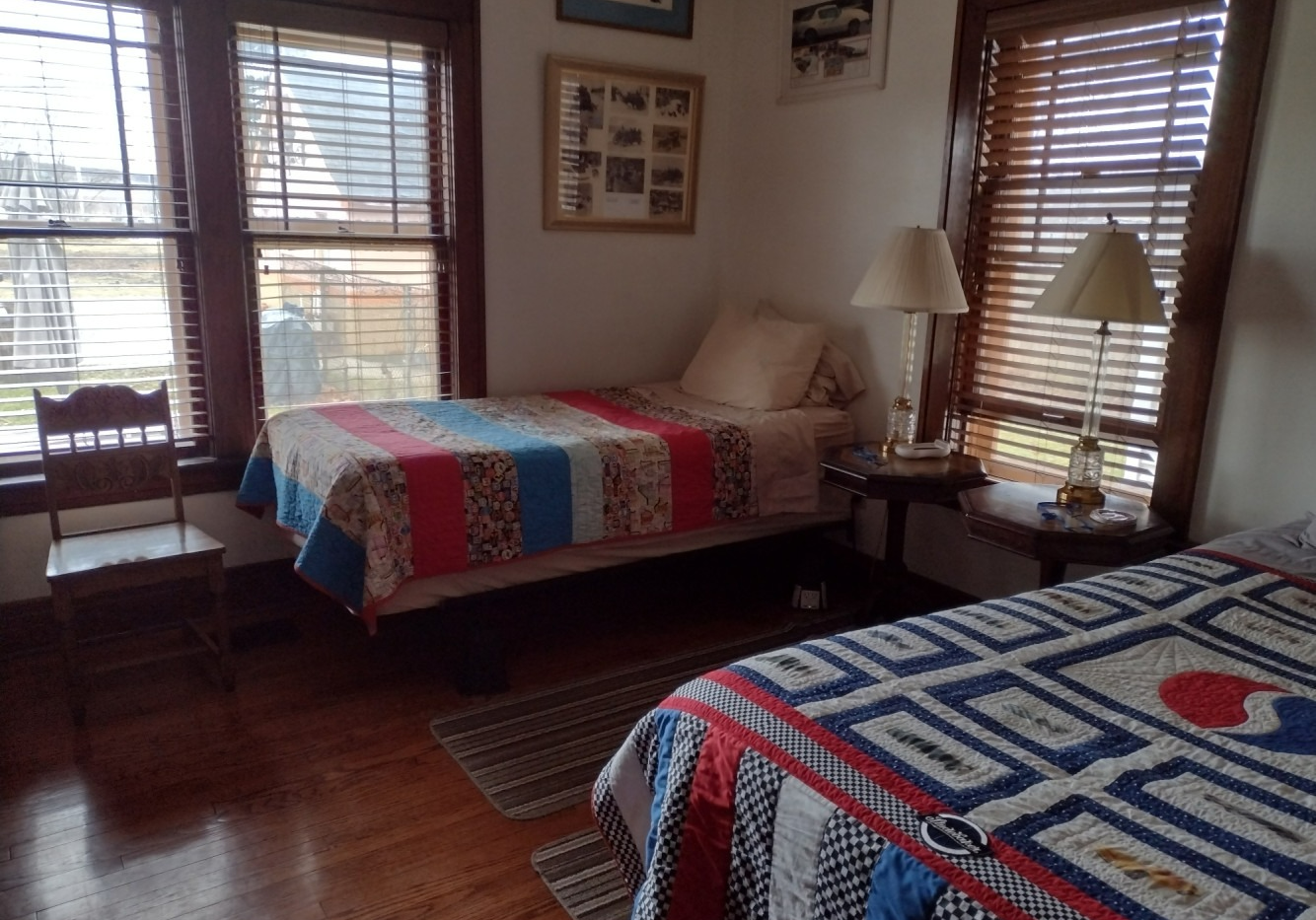 Bedroom with two twin beds, each with colorful quilts, wood floors, and a small table with lamps.
