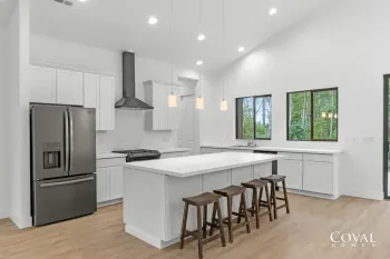 Bright modern white kitchen with island, stainless fridge, pendant lights, and wood floors