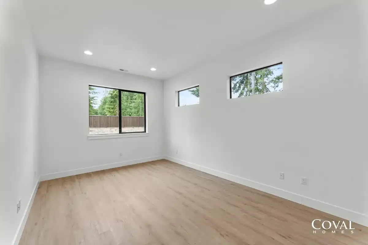 Empty white living room with light wood floors and three windows