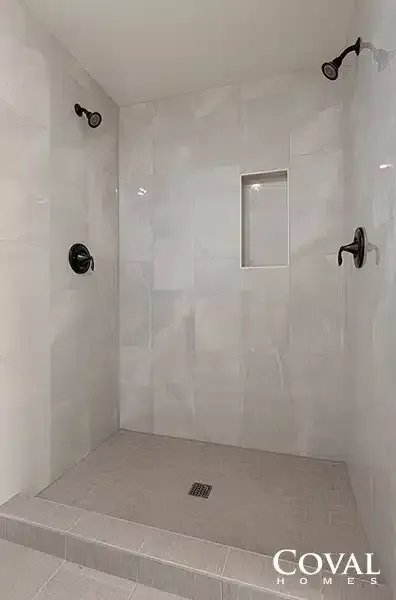 White tiled walk-in shower with multiple black fixtures and a recessed shelf.