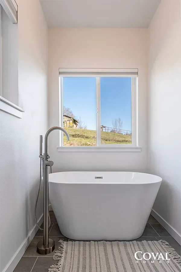 Small modern bathroom with a freestanding tub, window, and tall floor-mounted faucet.