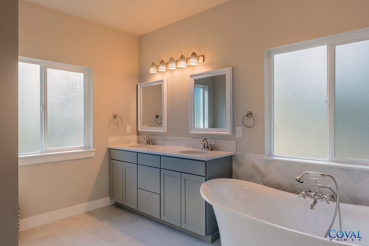 Bright bathroom with gray vanity, mirror lights, frosted windows, and a white bathtub.
