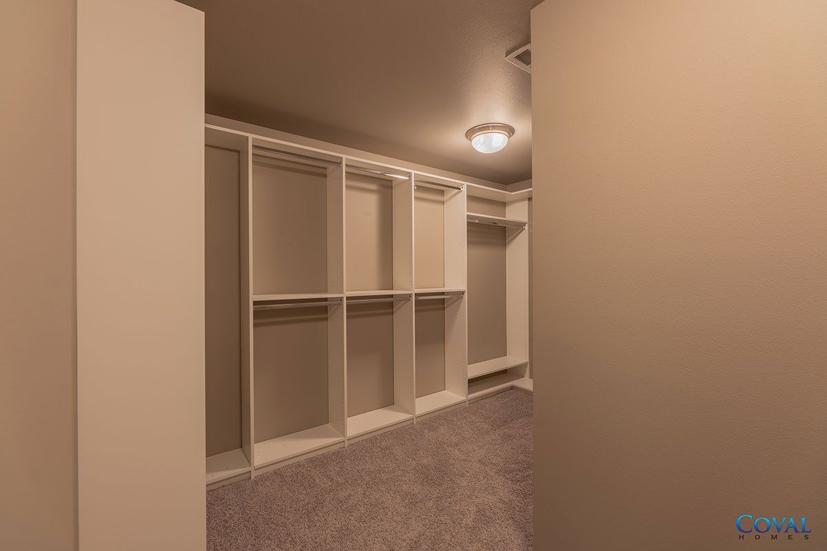 Empty walk-in closet with white shelving, beige walls, and carpeted floor under a ceiling light