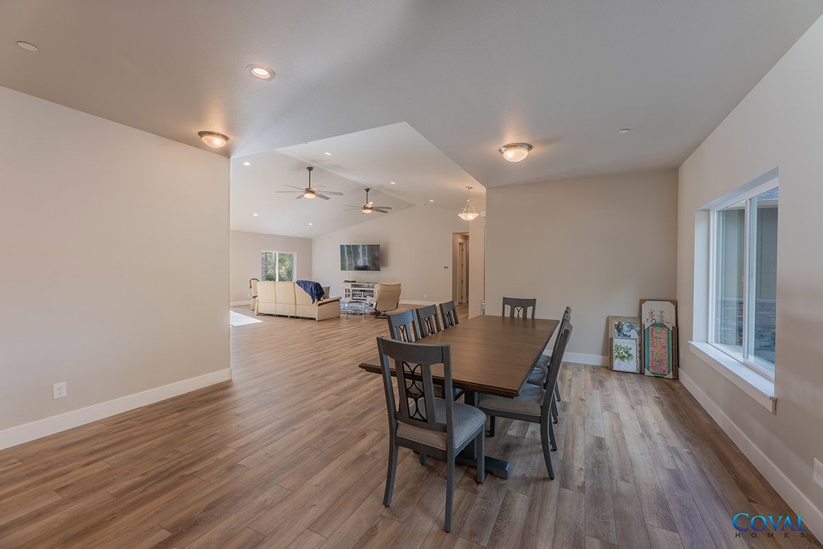 Bright open dining room with wood floors, long table, chairs, and a view into the kitchen/living area.
