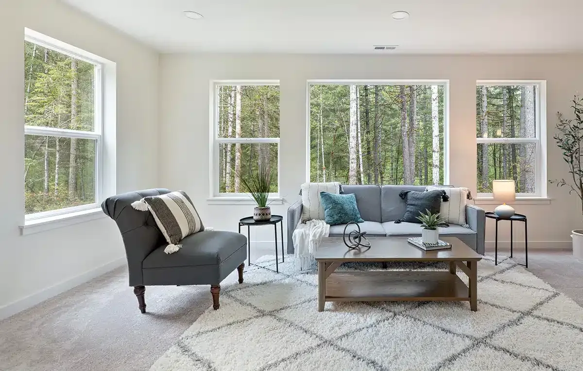 Bright living room with gray sofa, armchair, coffee table, and large windows overlooking trees
