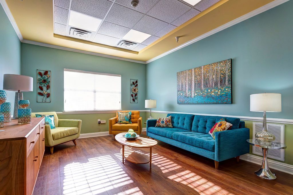 A living room with a blue couch , two chairs , a coffee table and a painting on the wall.