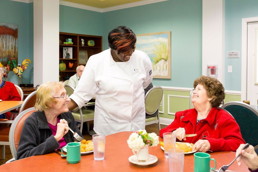 A chef is serving food to a group of elderly people sitting at a table.
