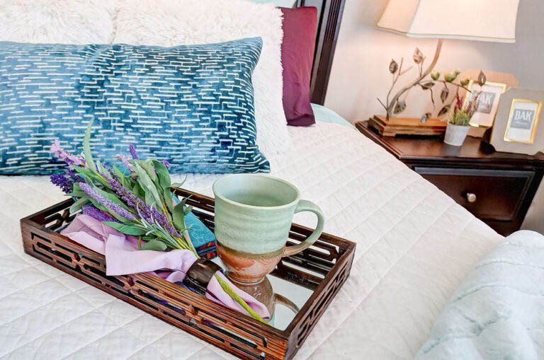 A tray with a cup of tea and flowers on it is on a bed.