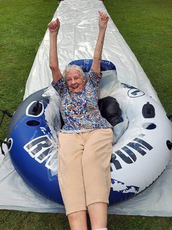 An elderly woman is sitting on an inflatable tube with her arms in the air.