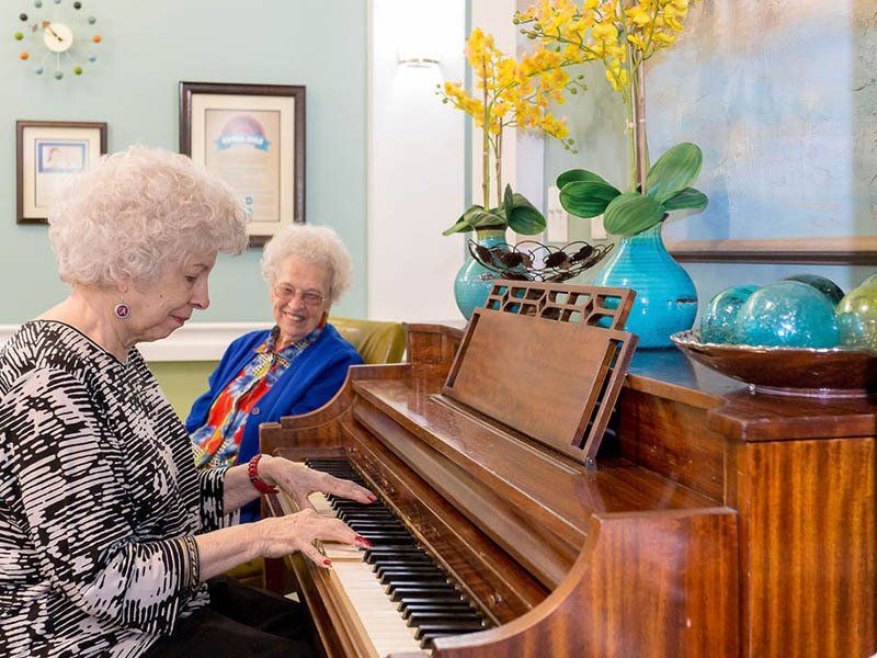 Two elderly women are playing a piano in a living room.