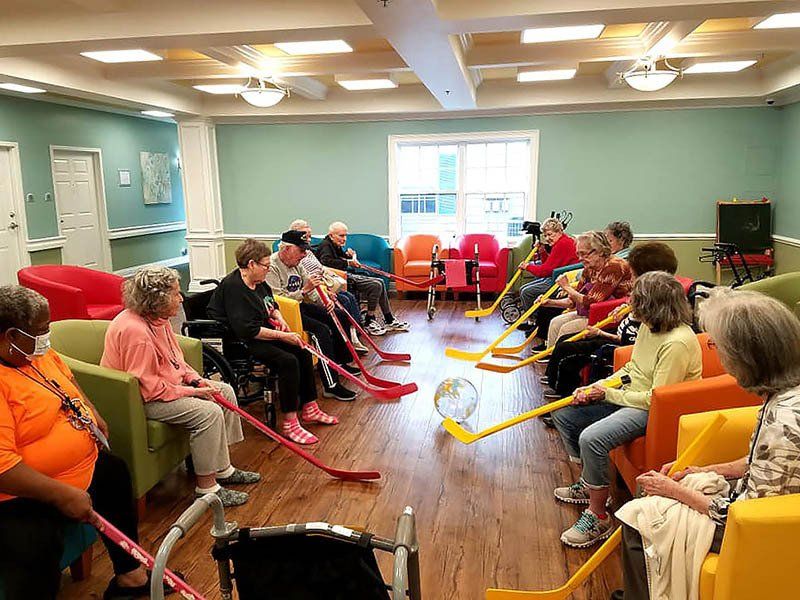 A group of elderly people are playing a game of ice hockey in a living room.
