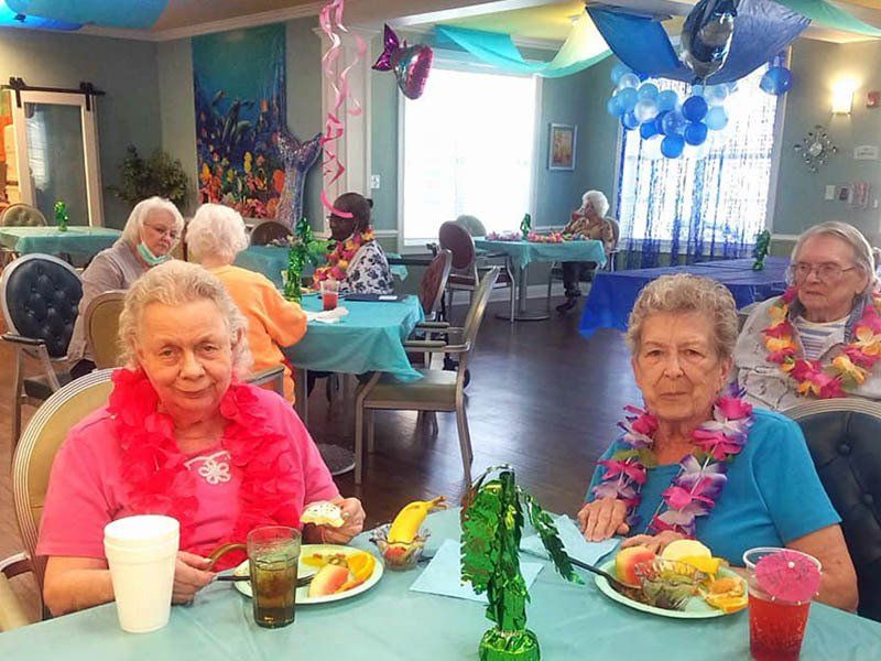 A group of elderly women are sitting at tables eating food.
