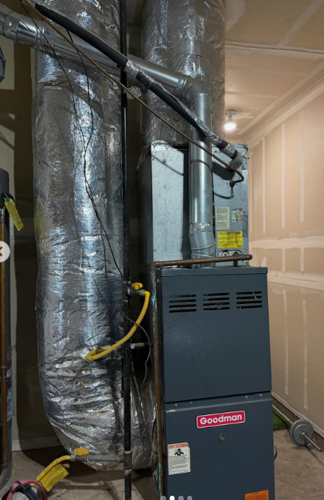 A Goodman furnace and HVAC system with silver insulated ductwork, standing in an unfinished room with drywall walls.