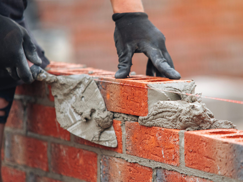 Gloved hands laying mortar on a red brick wall during construction