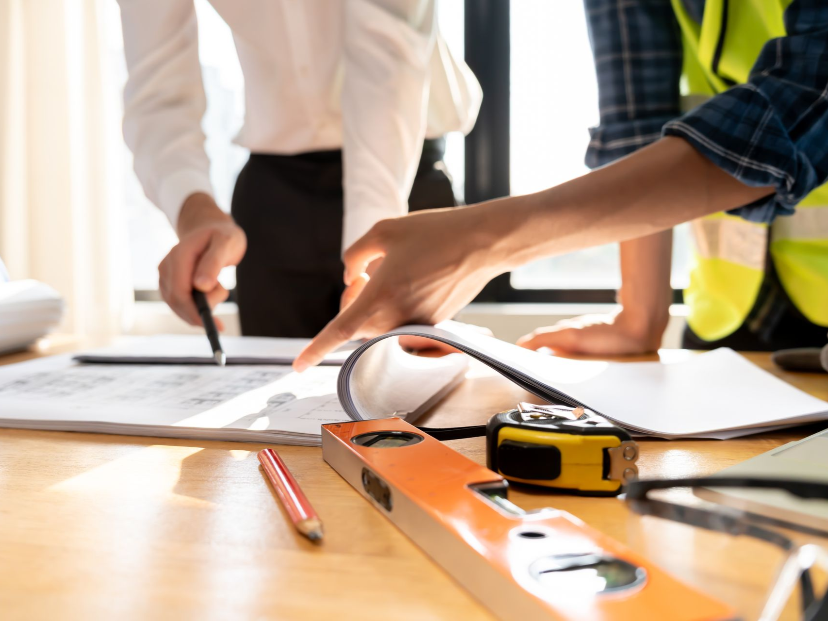 People reviewing blueprints and using tools on a construction table