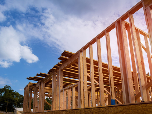 Wood-framed house under construction against a blue sky with clouds