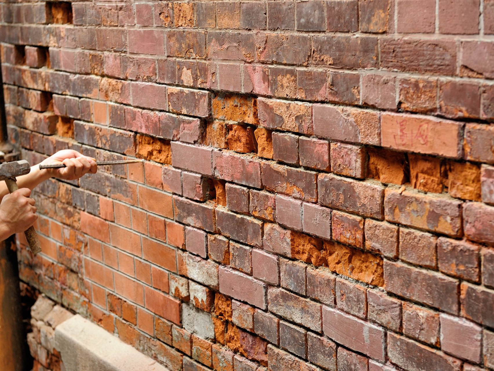 Hand removing damaged bricks from a cracked brick wall with multiple holes