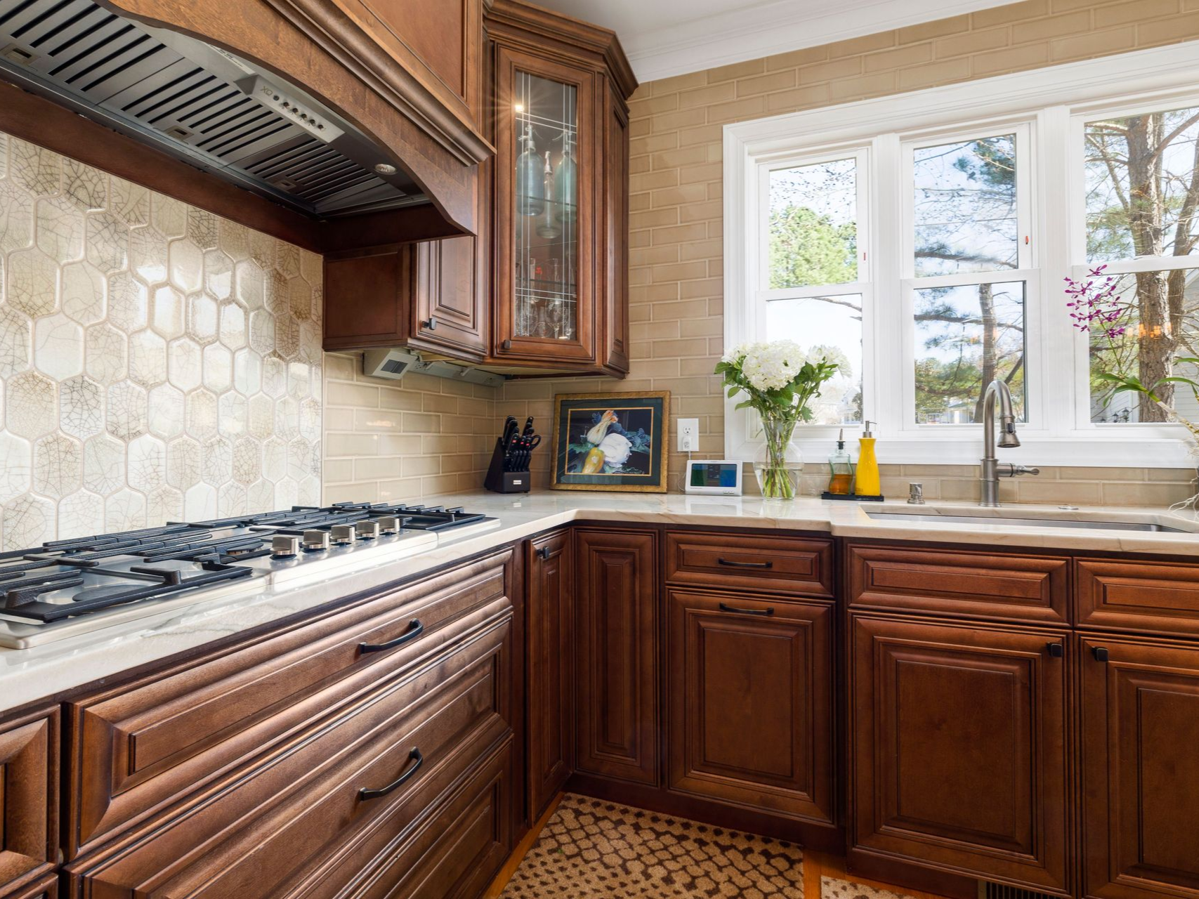 Kitchen with dark wood cabinets, gas stove, tiled backsplash, and a sunlit window over the sink.