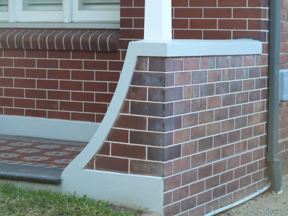 Brick house corner with a concrete ramp leading up to the porch.
