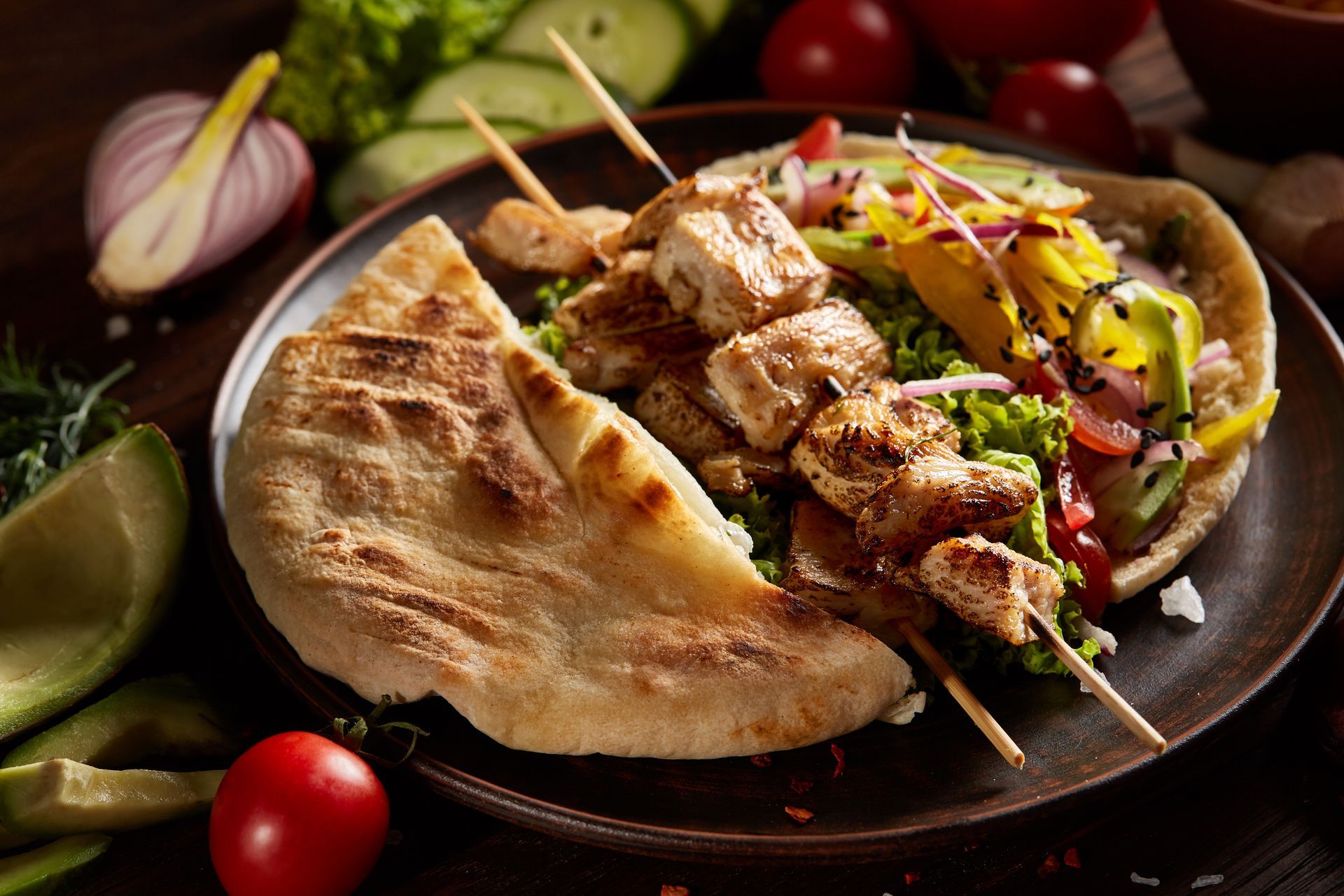 A plate of food with a pita bread and chicken skewers on a table.