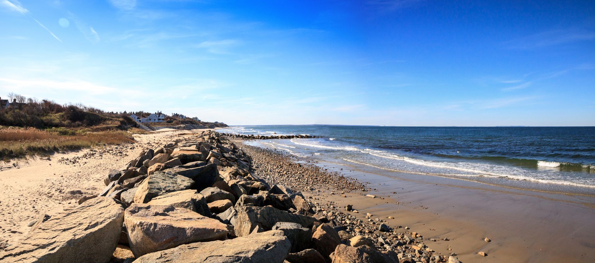 A beach with rocks and stairs leading to the ocean on a sunny day.