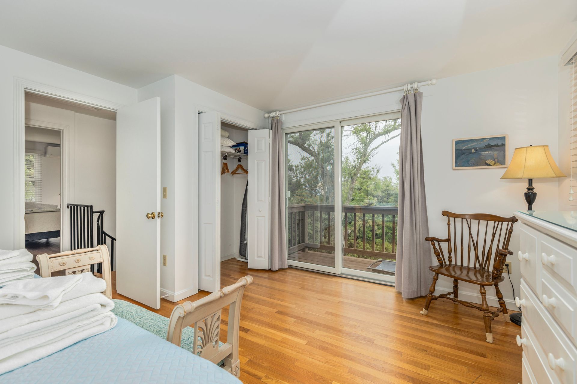 A bedroom with a bed , chair , dresser and sliding glass doors leading to a balcony.