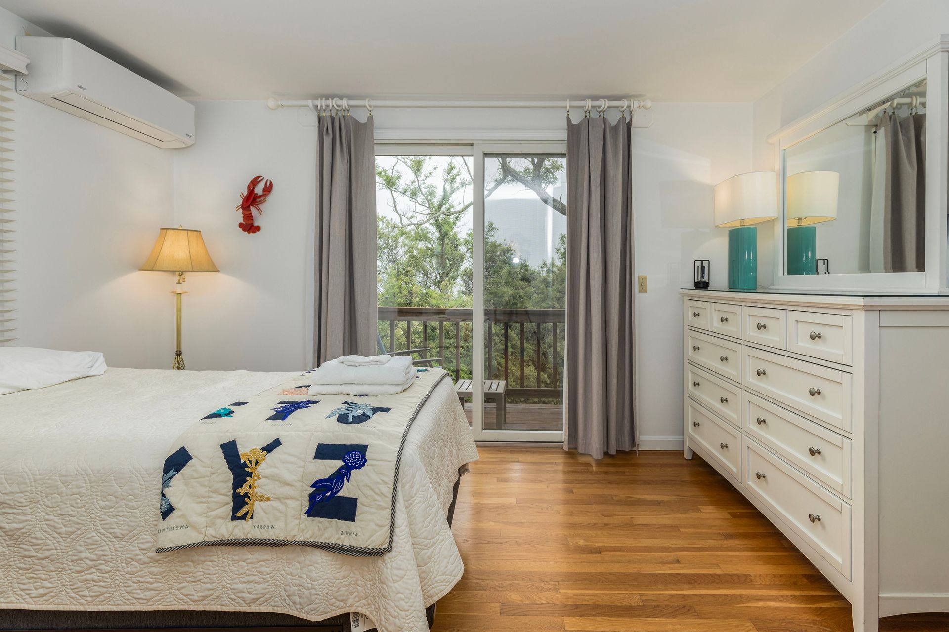 A bedroom with a bed , dresser , mirror and sliding glass door.